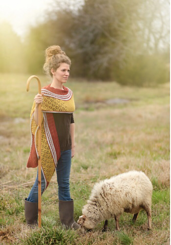 Shepherdess wearing knitted shawl and standing in a field with a grazing sheep