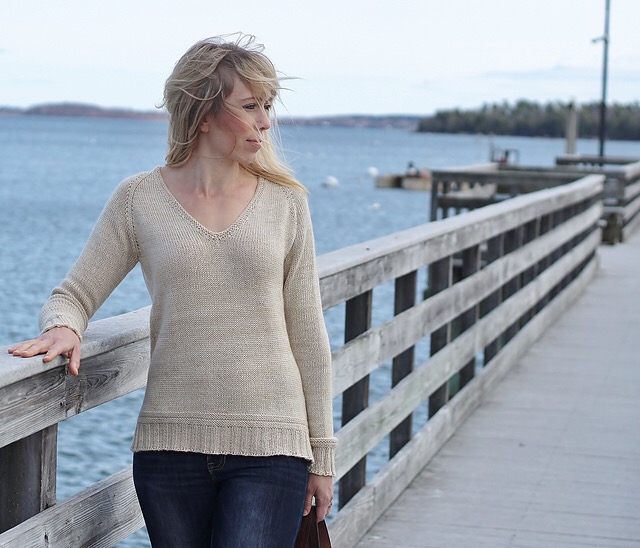 Blond light skinned woman wearing a hand knit ecru pullover while standing on a boat dock.