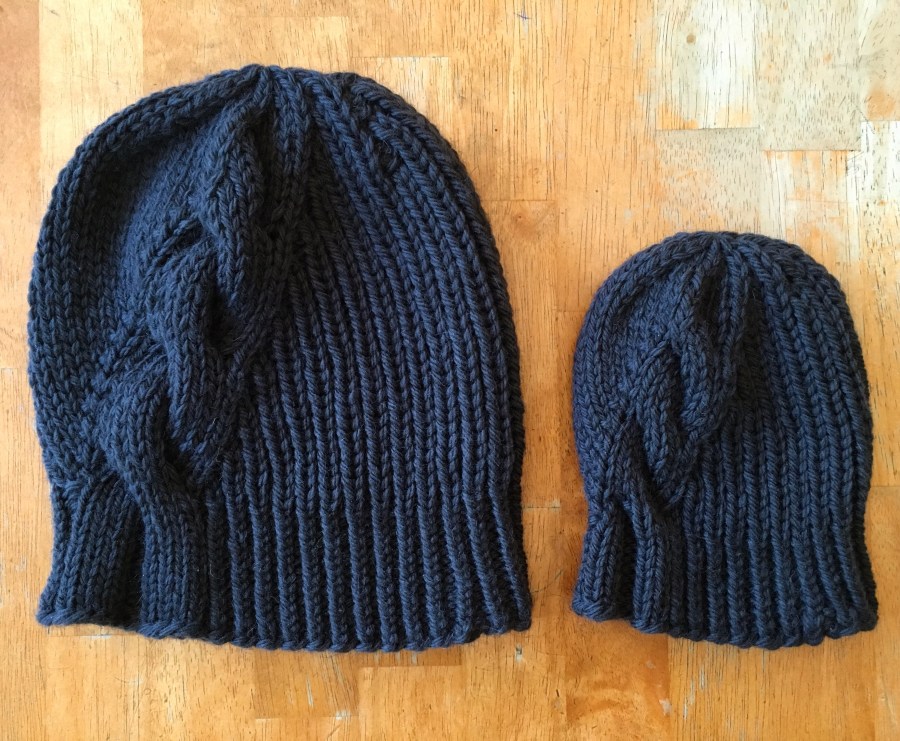 Two gray knit hats on a wooden table.