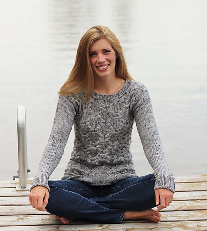 Woman wearing cabled sweater while sitting on a dock.