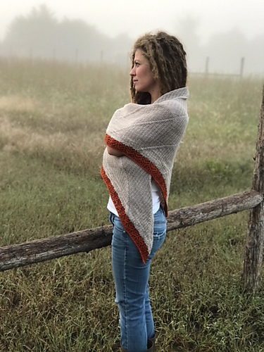 Woman wrapped in shawl and standing in a foggy field.